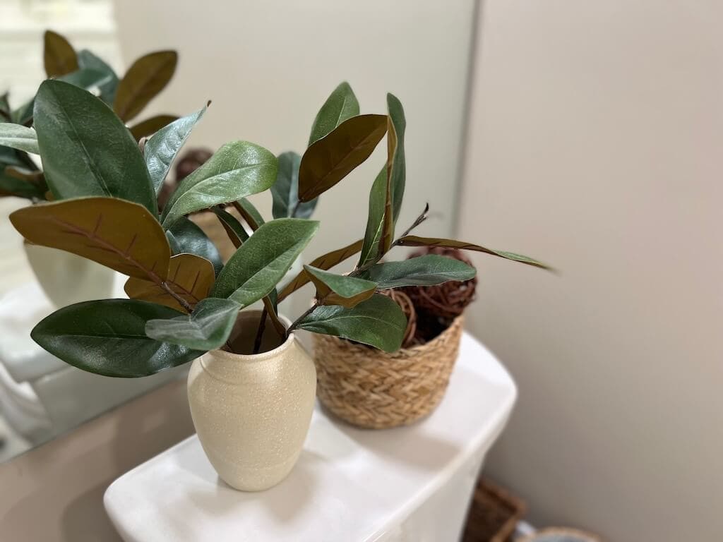 Decor on Toilet Tank in front of Large Sheet Mirror behind toilet